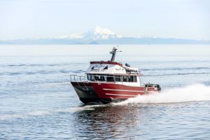 Red and white passenger boat cruising through calm waters with snow-capped mountains in background.