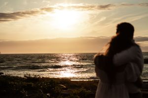 Silhouetted figures watching golden sunset over ocean horizon.