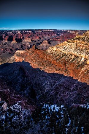 Panoramic view of the Grand Canyon with snow dusted ridges at sunset.