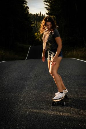 Figure skateboarding on empty road at sunset with forest backdrop.