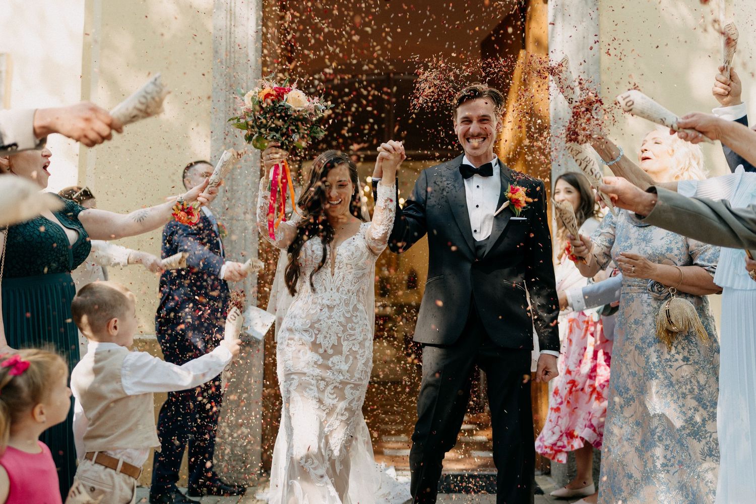 A bride and groom exit a church amid a golden confetti celebration with guests.