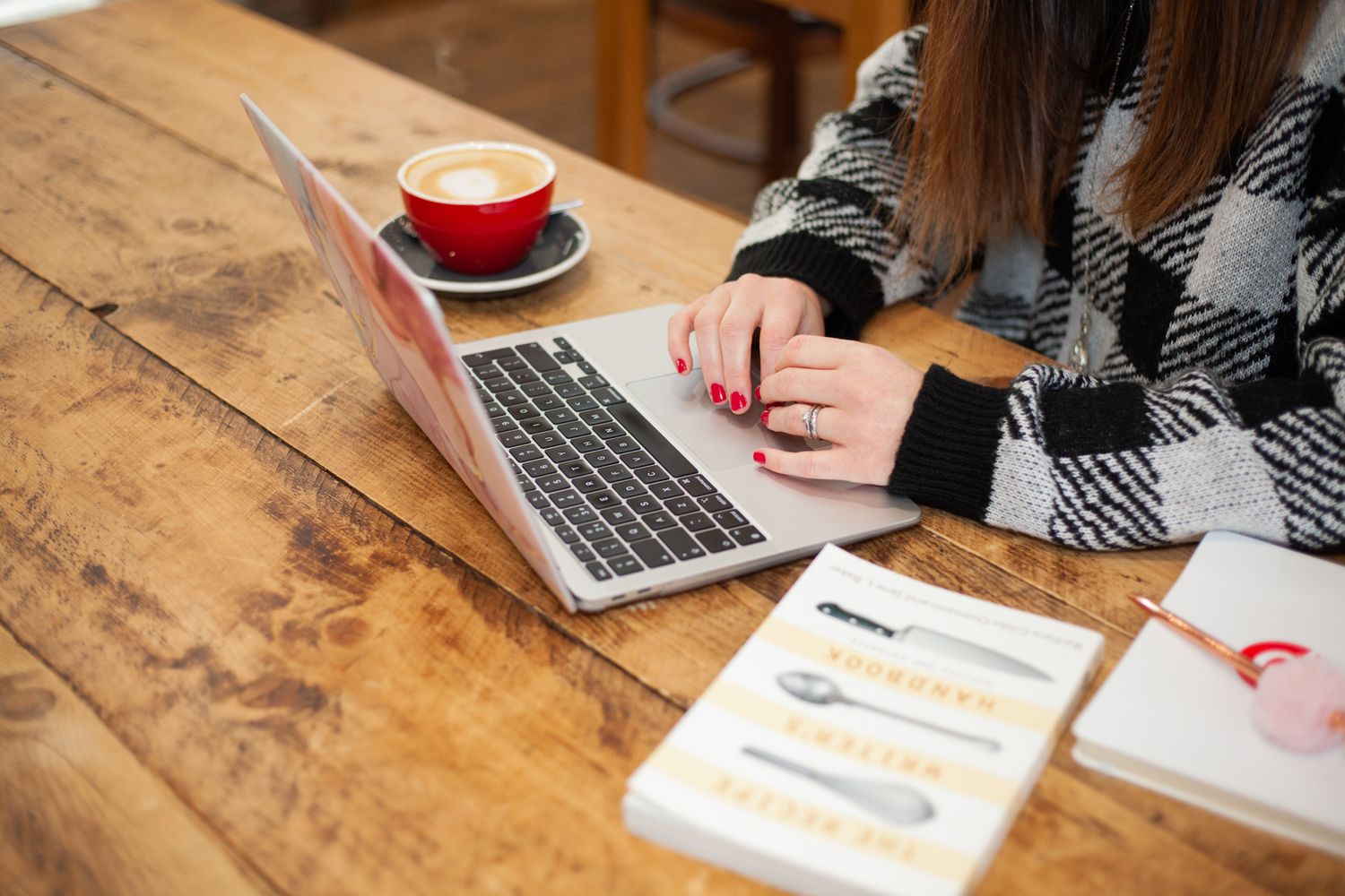 image of a woman typing on a laptop surrounded by reference books and a red coffee cup.
