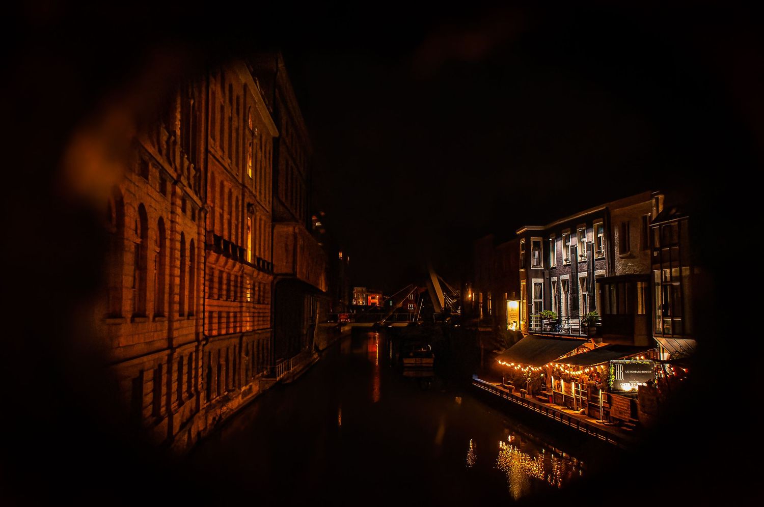 Nighttime photo of an illuminated historic European canal or street with buildings reflecting in the water. Gent belgium
