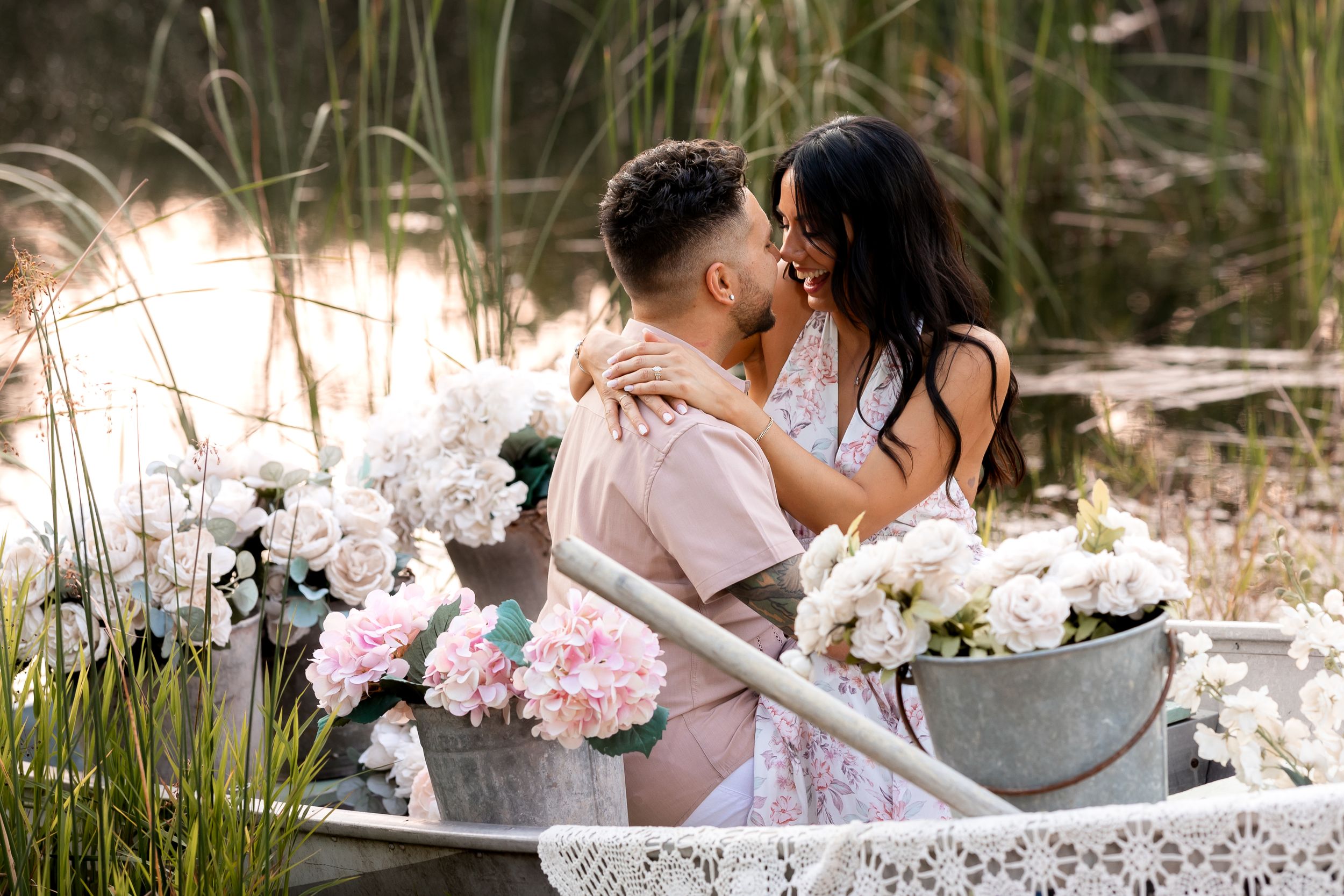 Romantic couple pose in rowboat surrounded by pink floral arrangements.