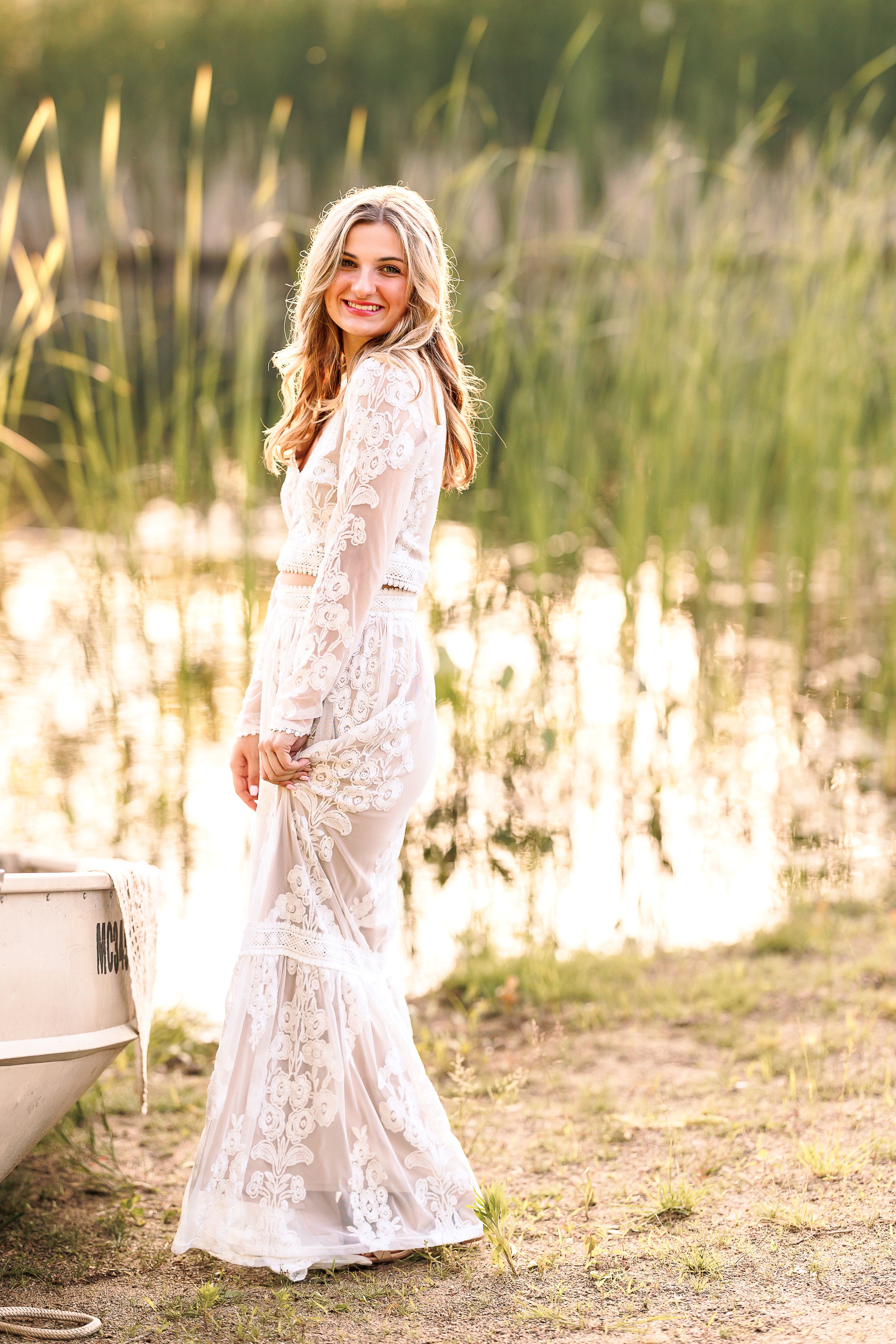 A white lace dress flows elegantly in a natural outdoor setting during a golden hour photoshoot.