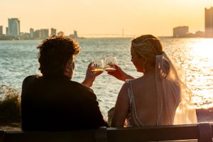 Silhouettes of people enjoying sunset over water with city skyline in background.