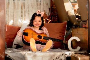 A small child sits on a couch with an acoustic guitar in a cozy home setting.