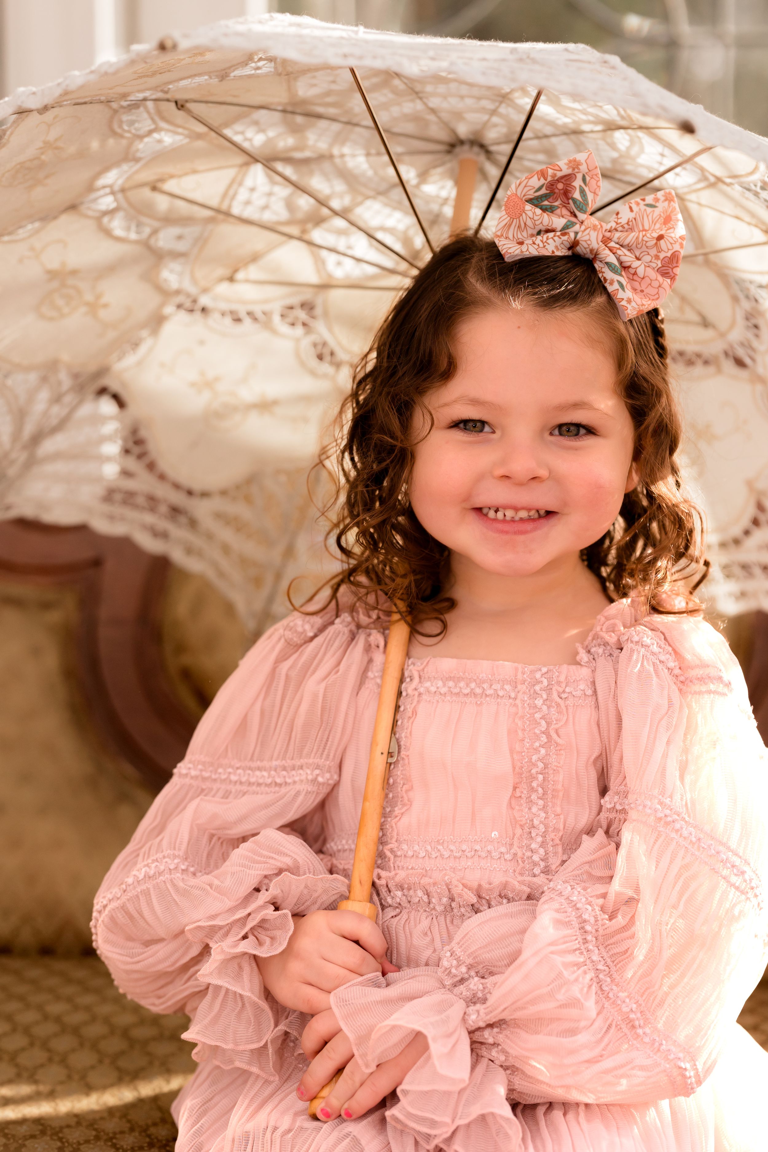 A child in a pink dress poses with a vintage lace parasol against a light background.