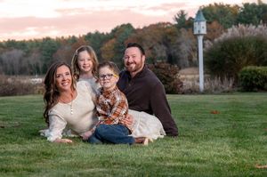 A family sits together on grass at sunset with a birdhouse visible in the background during autumn.