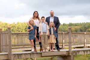 A happy family stands together on a wooden boardwalk against a natural backdrop on a cloudy day.