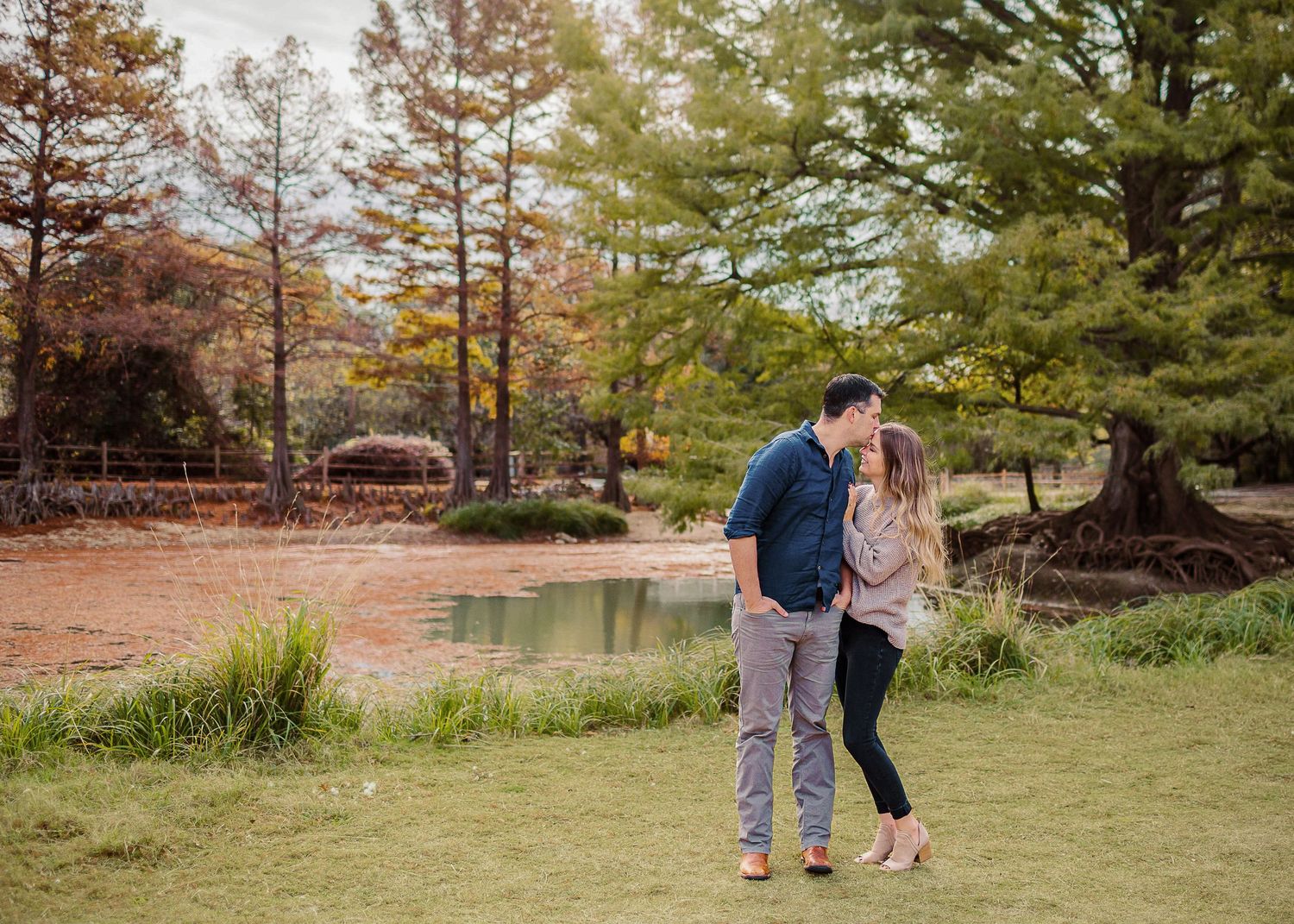 Couple standing together near a scenic pond surrounded by autumn trees, by best San Antonio Photographer.