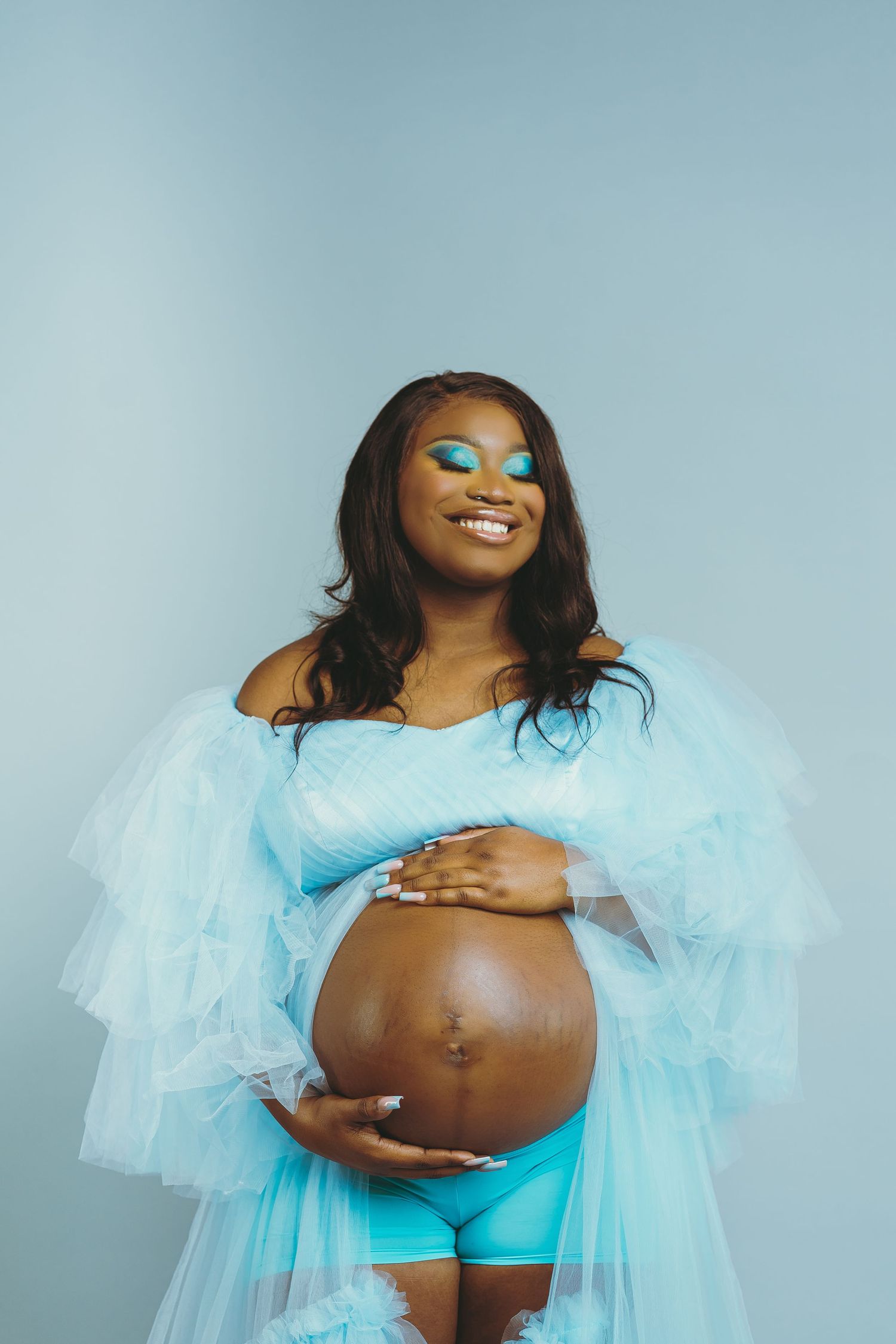 Maternity photo featuring person in light blue tulle dress against pale blue background.