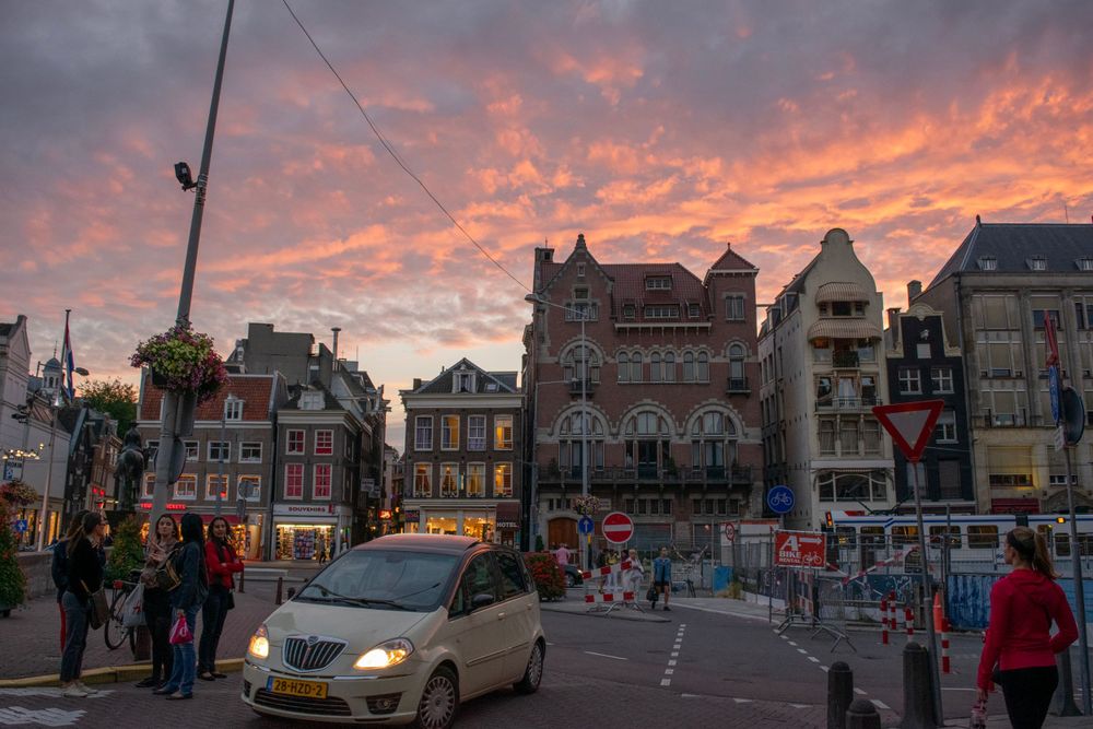 Dramatic sunset sky over Amsterdam streets with historic buildings and evening traffic.