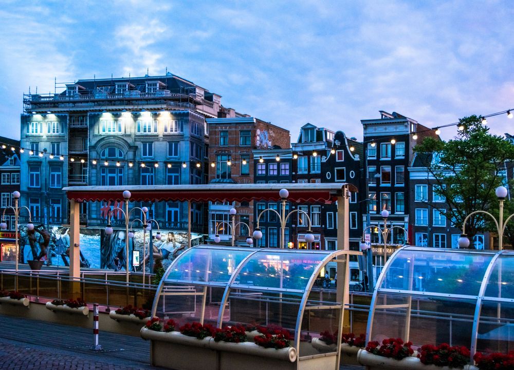 Modern glass domes and blue-lit buildings along Amsterdam waterfront at dusk.