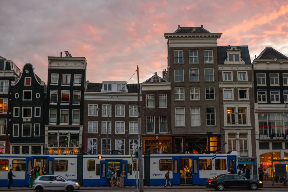 Amsterdam canal houses at sunset with characteristic Dutch architecture and a passing tram.