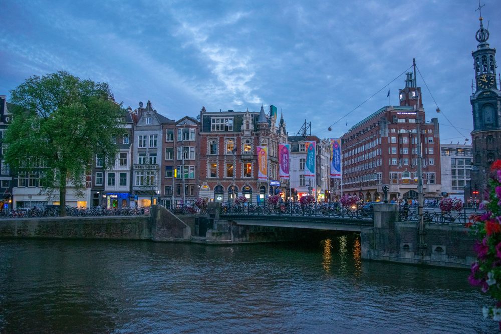 Historic buildings along Amsterdam's canal with colorful flags and evening lighting.