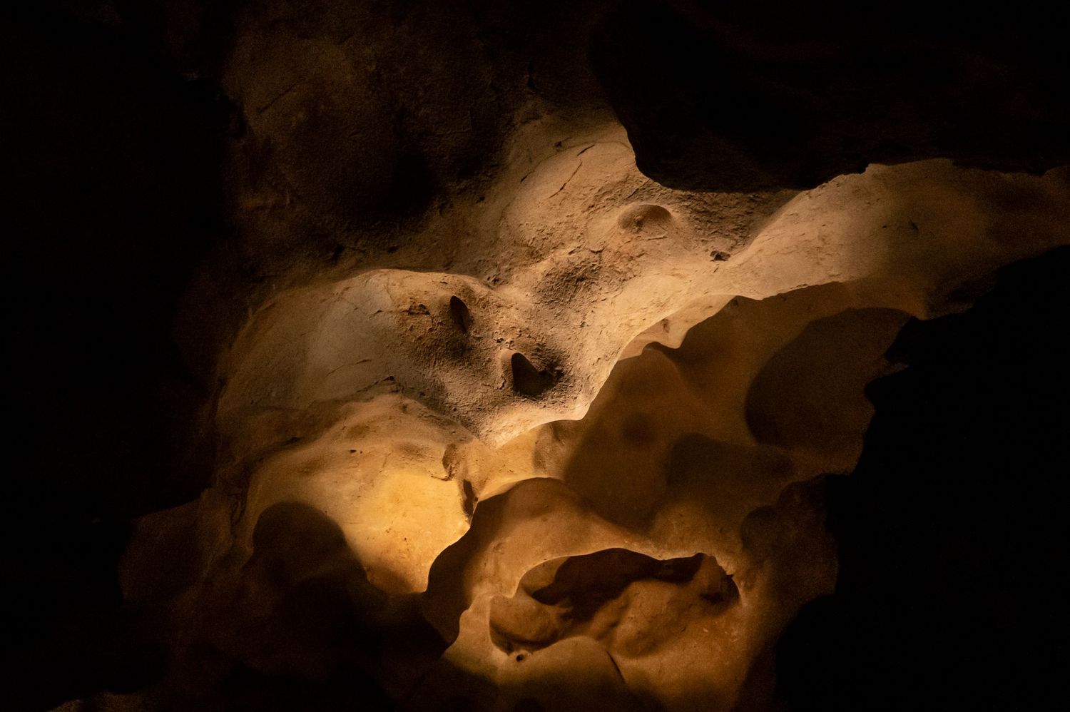 Dramatic illuminated rock formations in a dark cave create an ethereal atmosphere with warm glowing light.