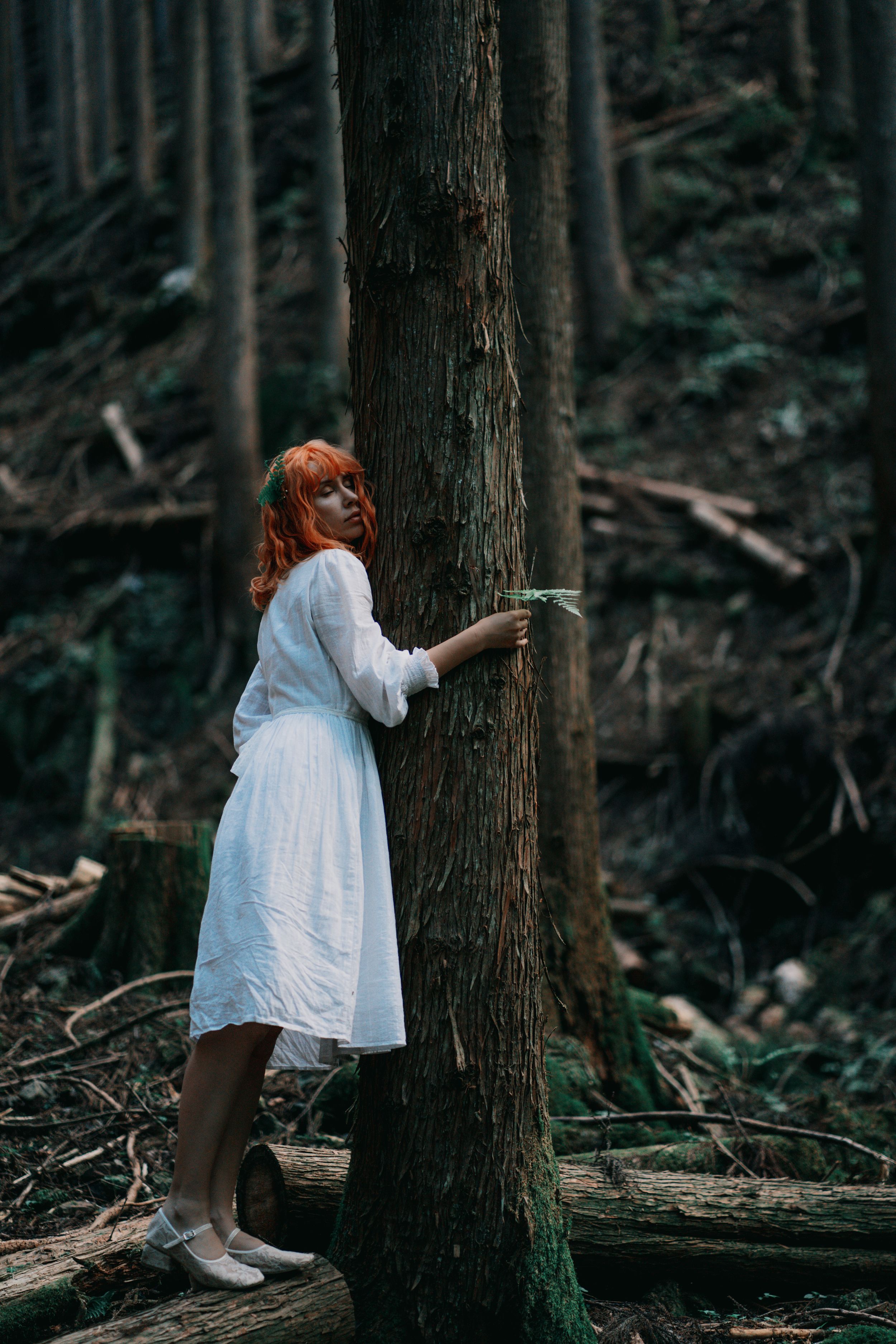 Creative portrait of a red-haired girl hugging a tree in the forest