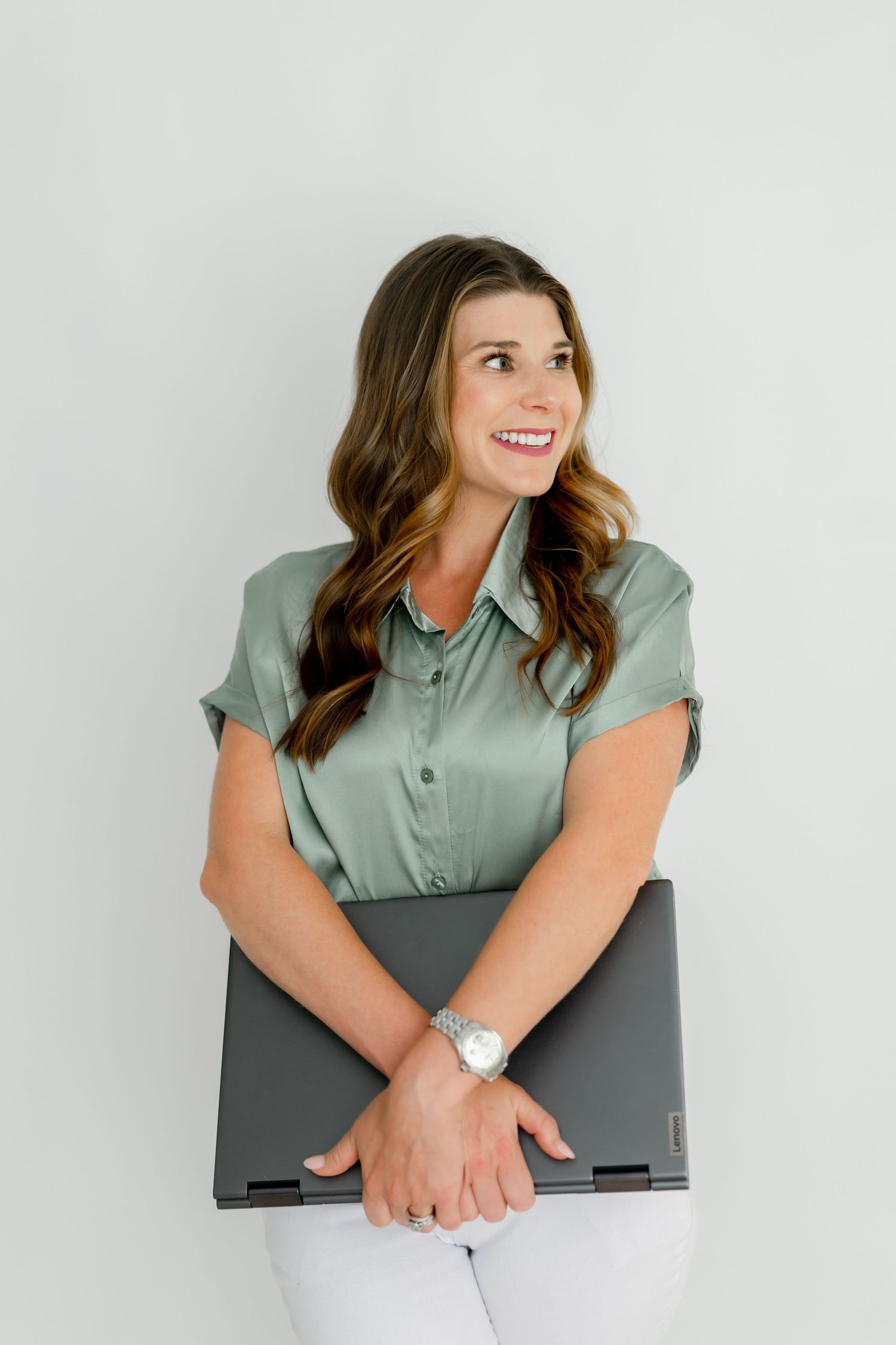 Business professional holding laptop while wearing sage green blouse against white wall.