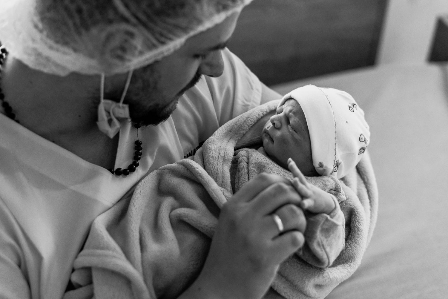 padre con cofia y barbijo son sus bebe recién nacido tocando su mano en habitación de sanatorio donde nació