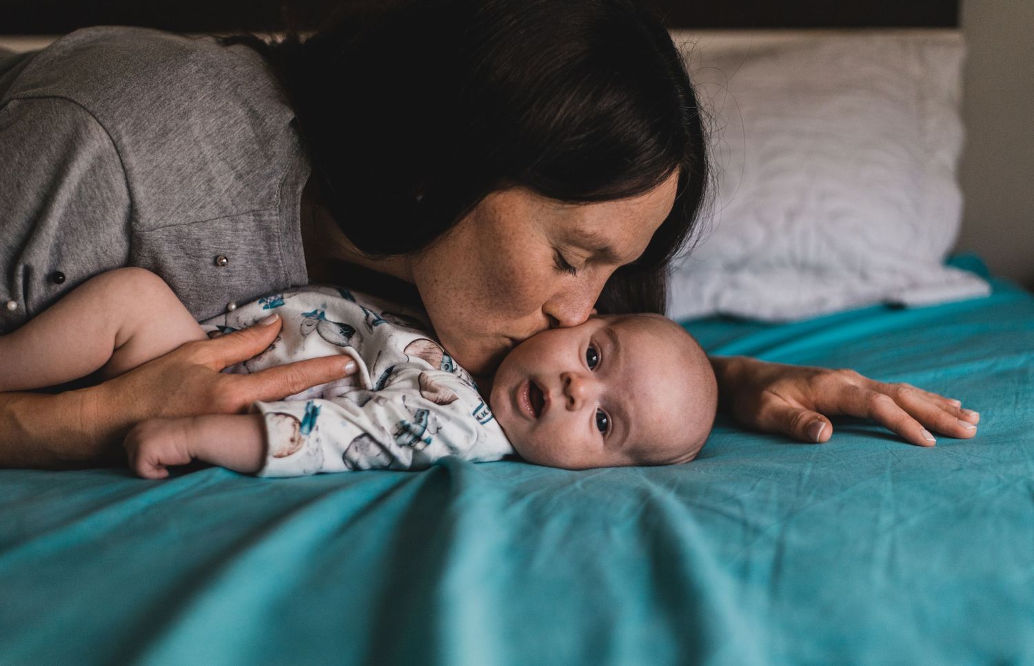 bebé recién nacido acostado sobre la cama de sus padres, su mamá asoma sobre el y lo besa