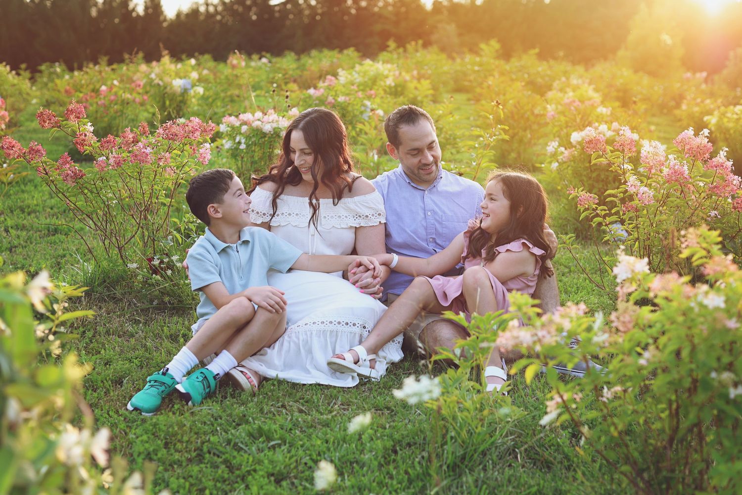 A family sits together in a flower garden during golden hour sunset.