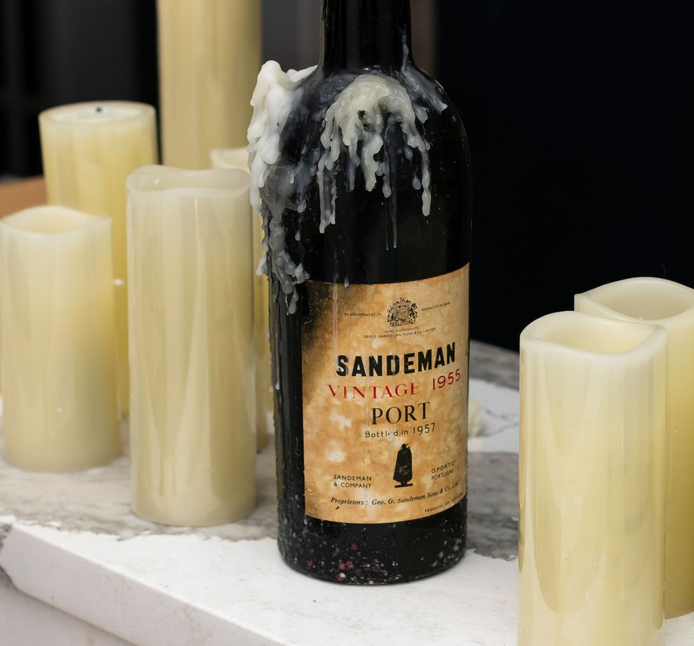 Sandeman port wine bottle surrounded by white candles on display.