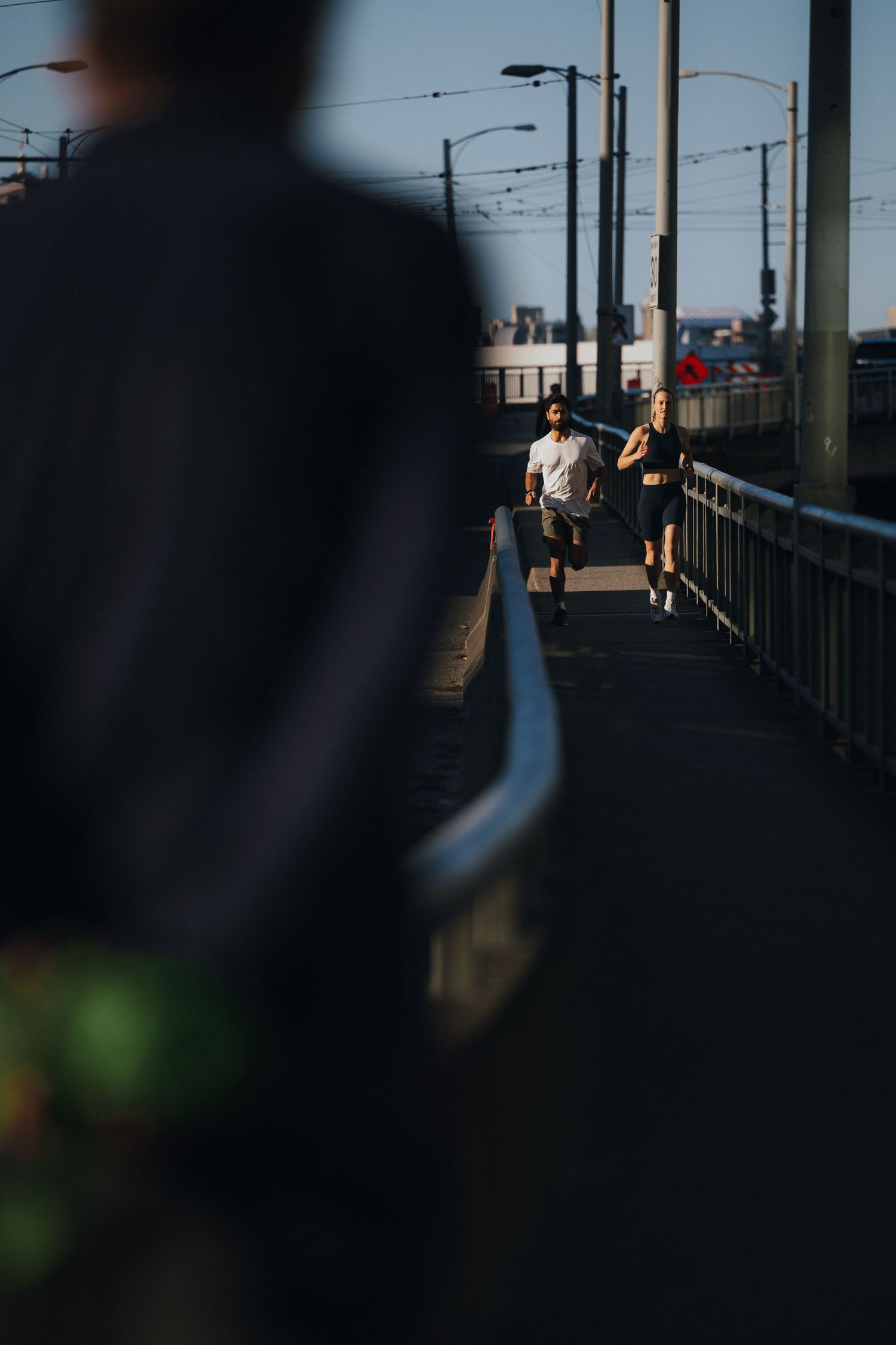 Silhouetted figures walking on bridge with urban infrastructure in background.