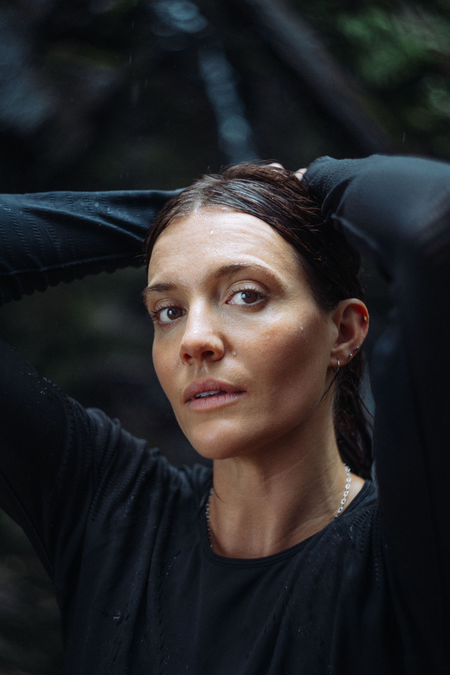 A close-up portrait in moody lighting wearing a black outfit against a dark background.