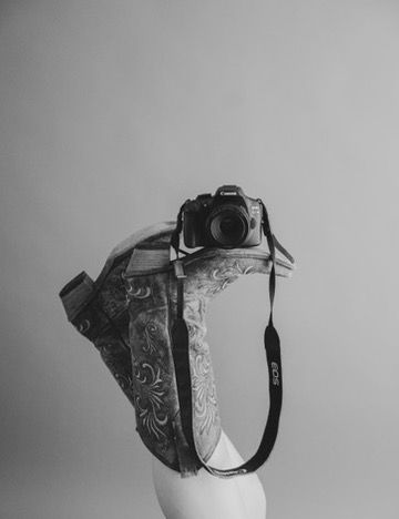 Black and white studio picture, branding session, cowboy boots and camera, western vibes.