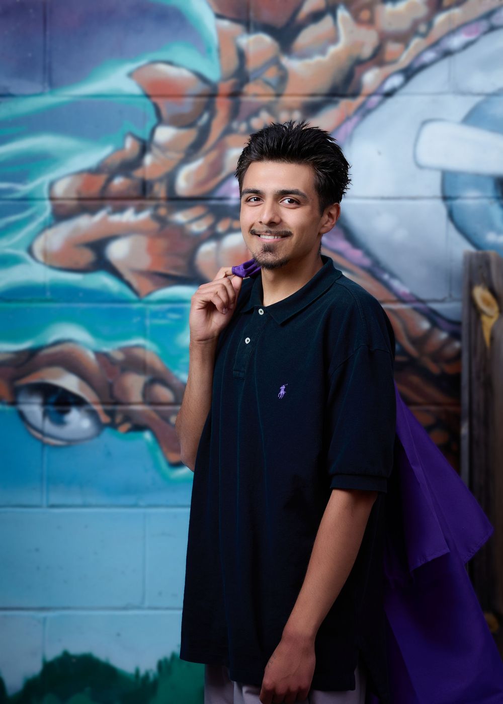 A young person in a black polo shirt poses smiling against a colorful graffiti wall background.