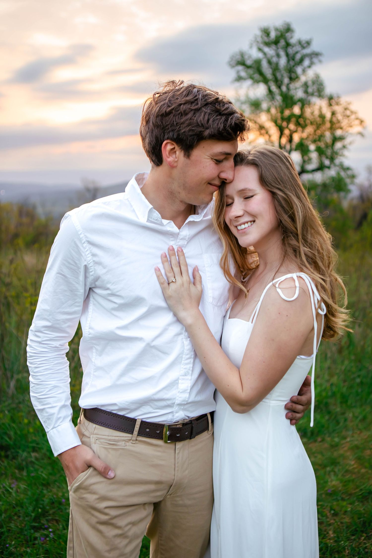 A romantic couple embraces in a field during sunset wearing white and khaki wedding attire.