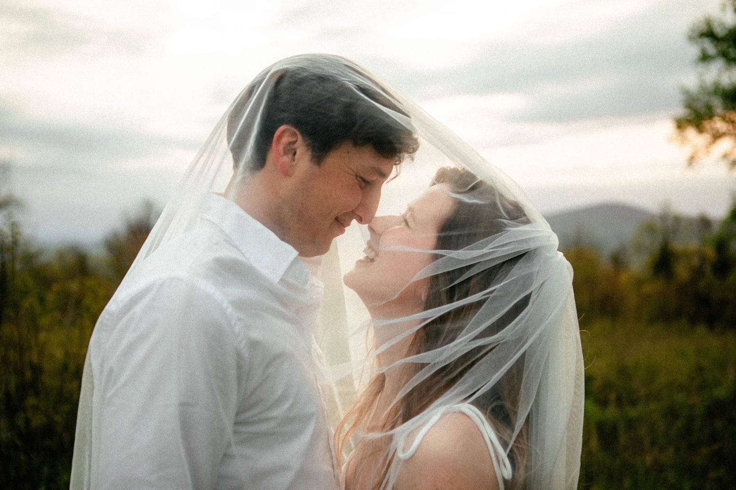 Romantic outdoor wedding portraits with flowing veil against sunset sky.