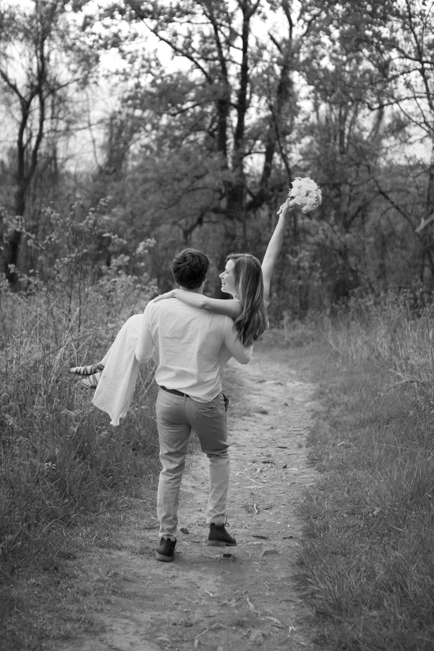 Black and white photos of couple dancing playfully on nature trail.