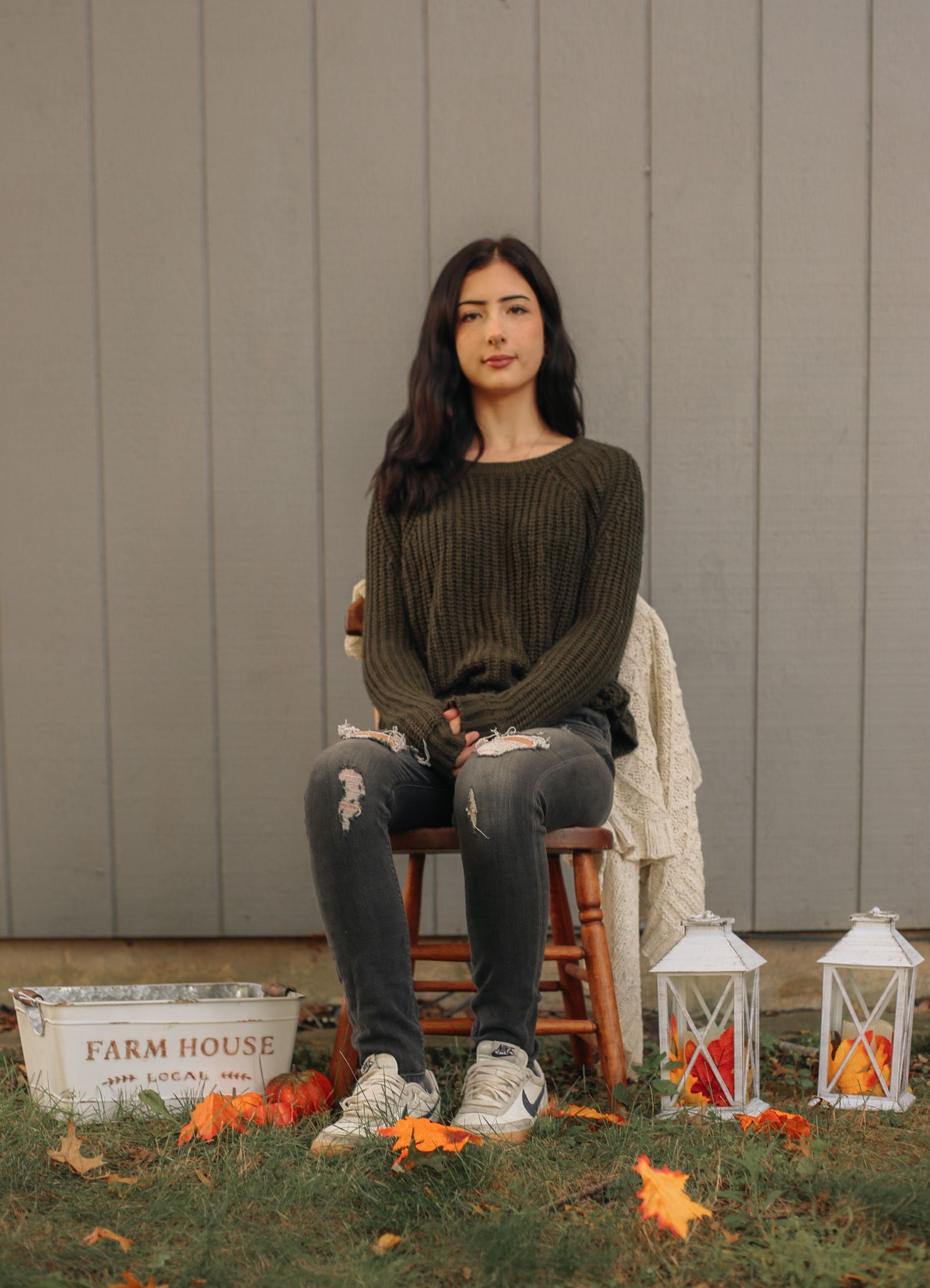 Fall themed outdoor portrait session with pumpkins and lantern decorations against gray wall.