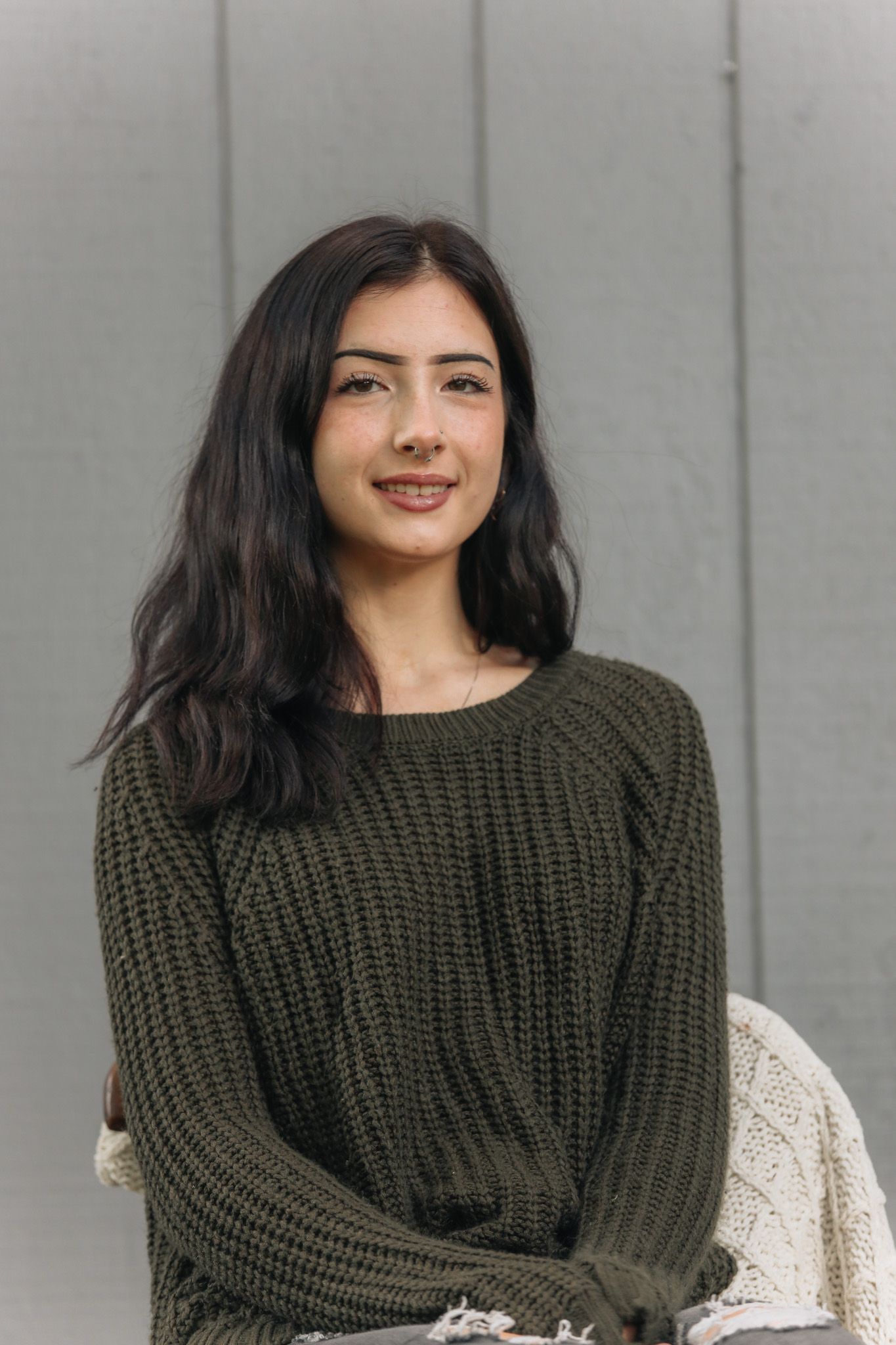 Woman wearing olive green sweater poses against grey wall in casual portrait series.