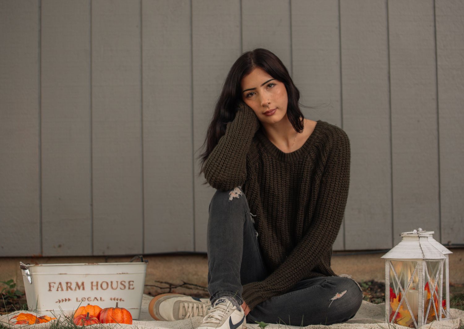 Woman in dark sweater sits at farmhouse table with fall decor.