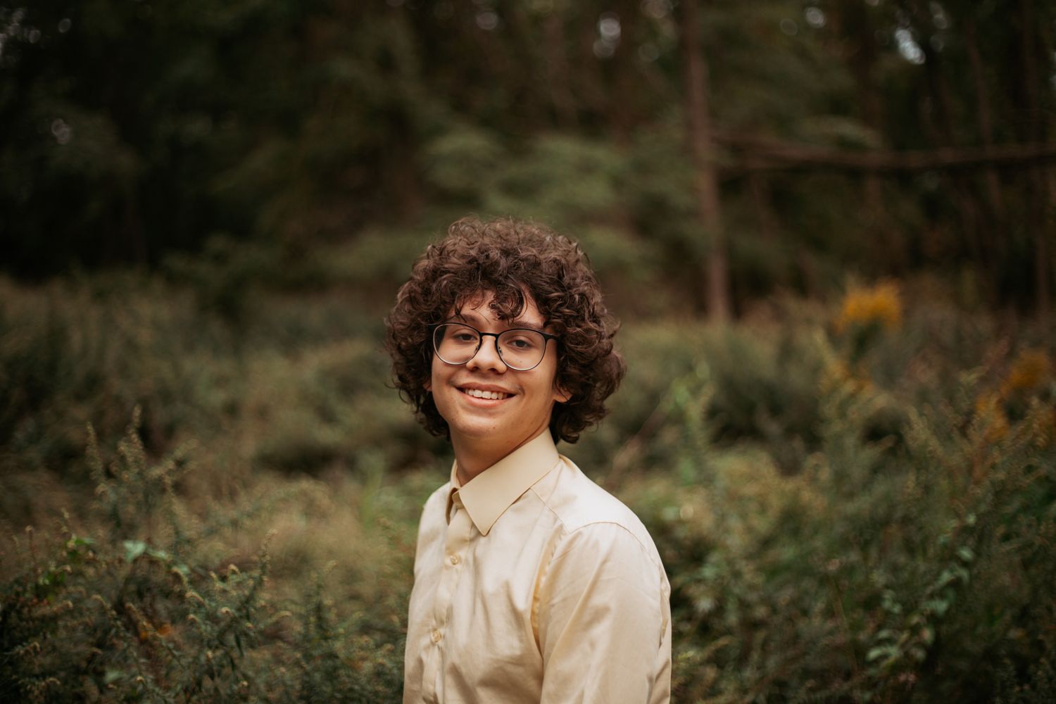 Portrait of someone in a light button-down shirt against a natural outdoor background.