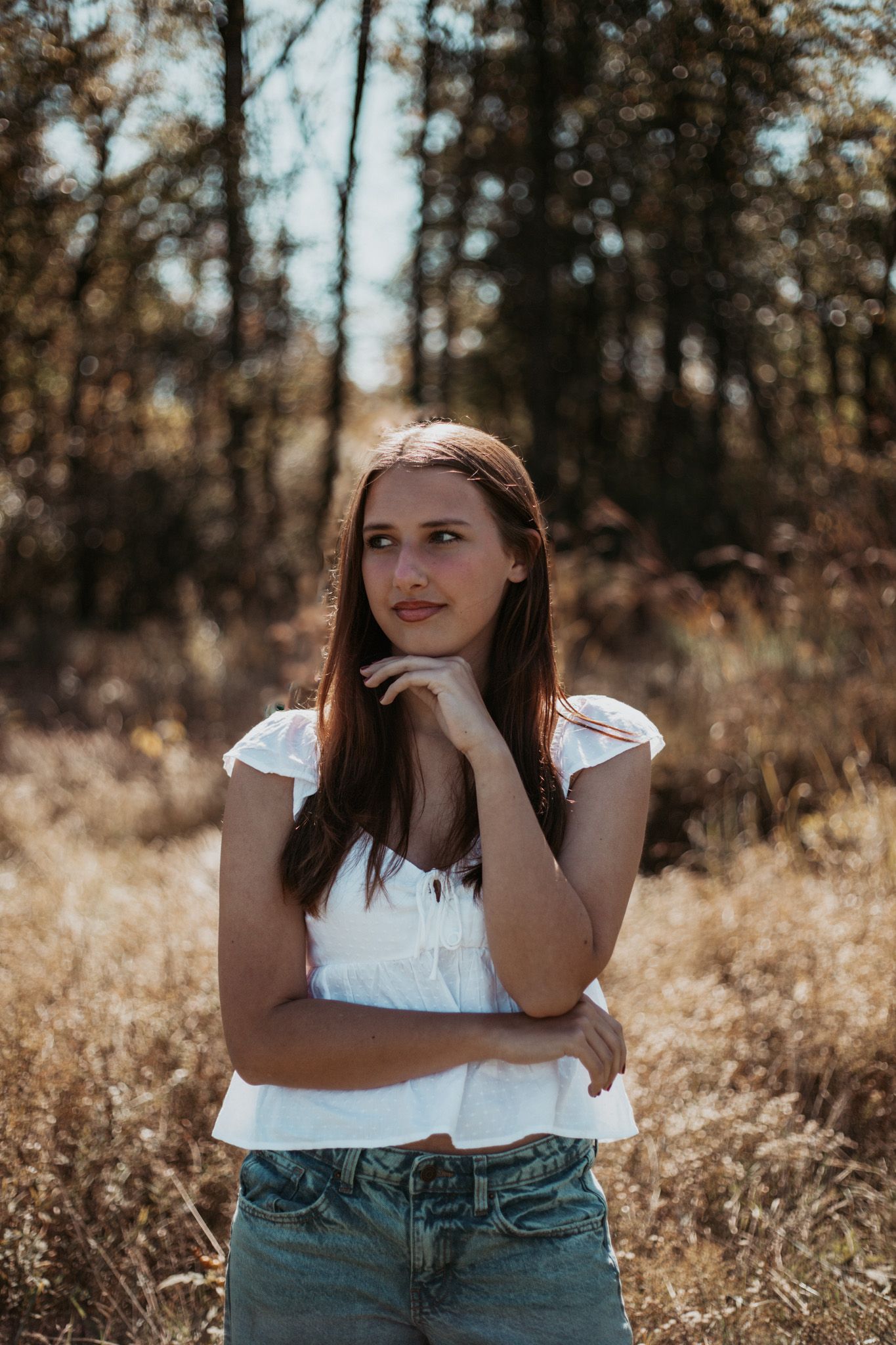 Portrait of someone in white top and jeans standing in golden autumn field.