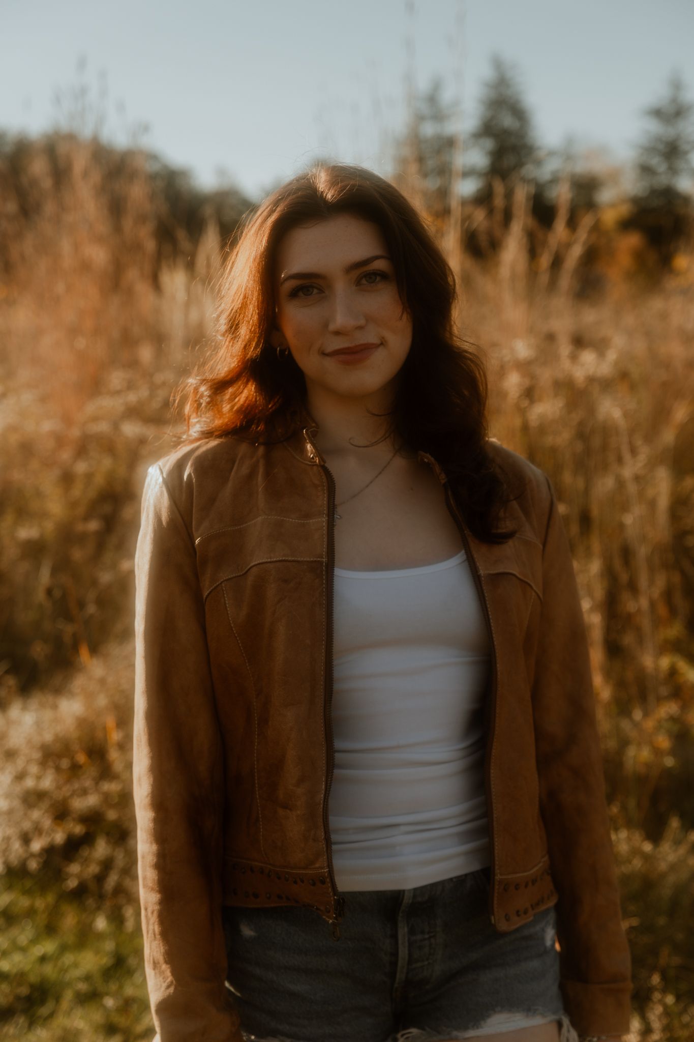 A golden hour outdoor scene with tall grass and autumn colors in the background.