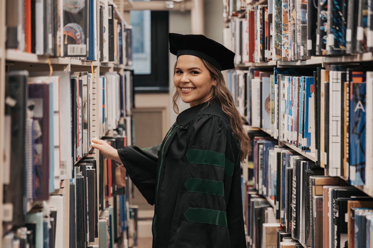 A person in a green uniform reaches for books on tall library shelves.
