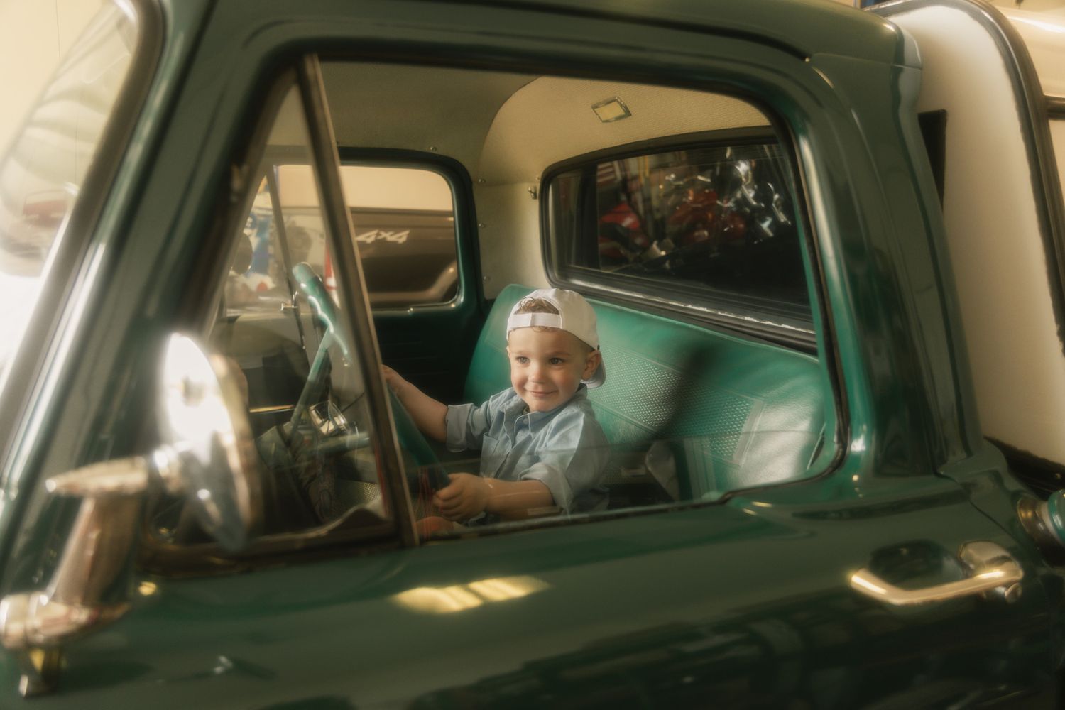 A person sits in the driver's seat of a car, viewed through multiple window reflections.