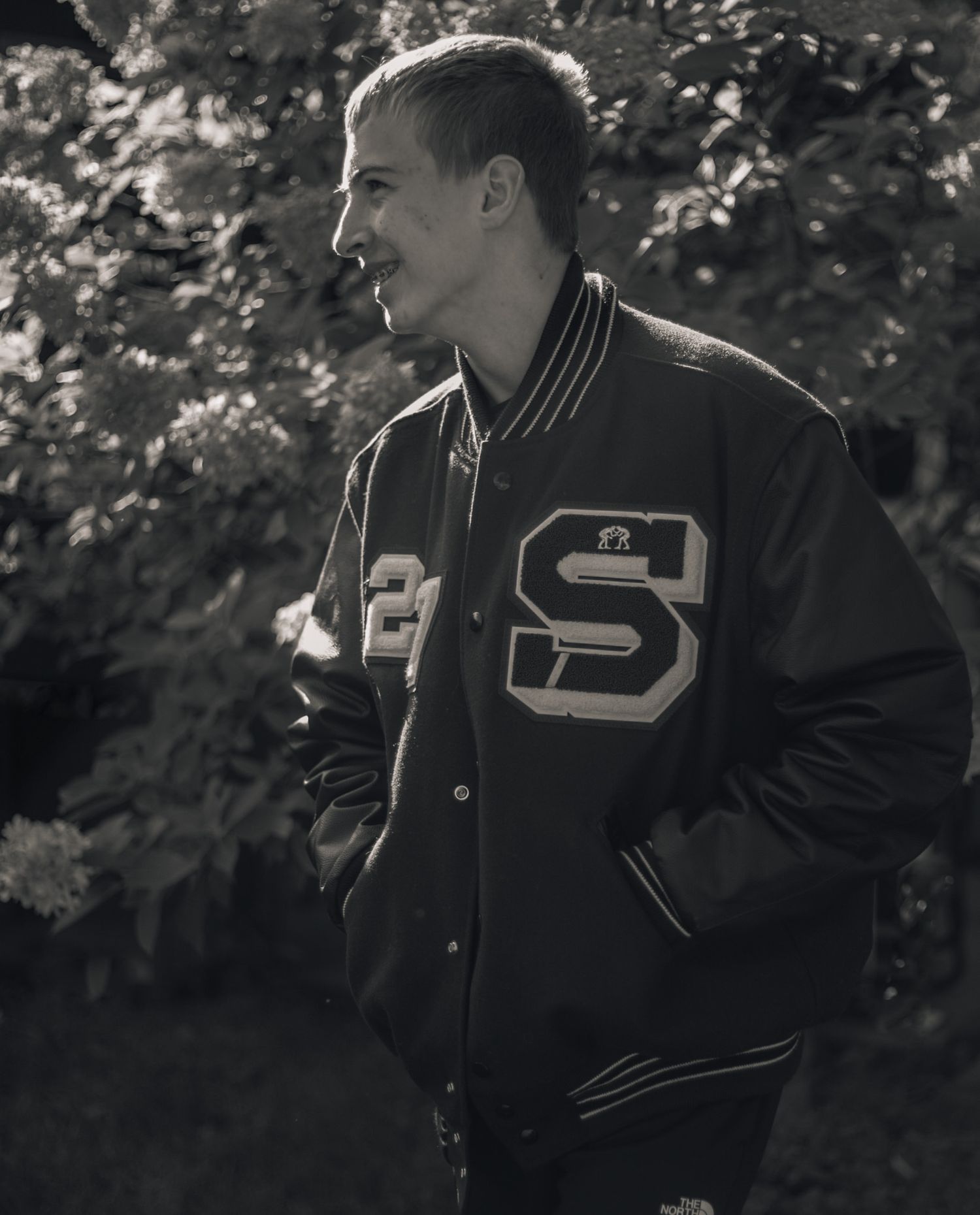 Person wearing letterman jacket poses against blurred outdoor background.