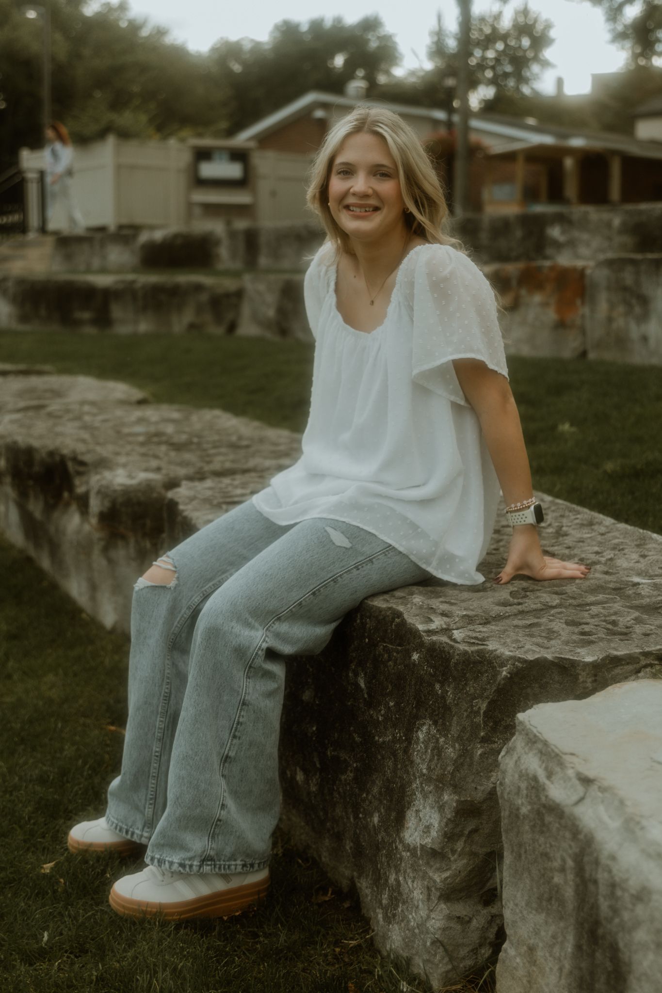 Person in casual attire sitting on stone wall in rustic outdoor setting.