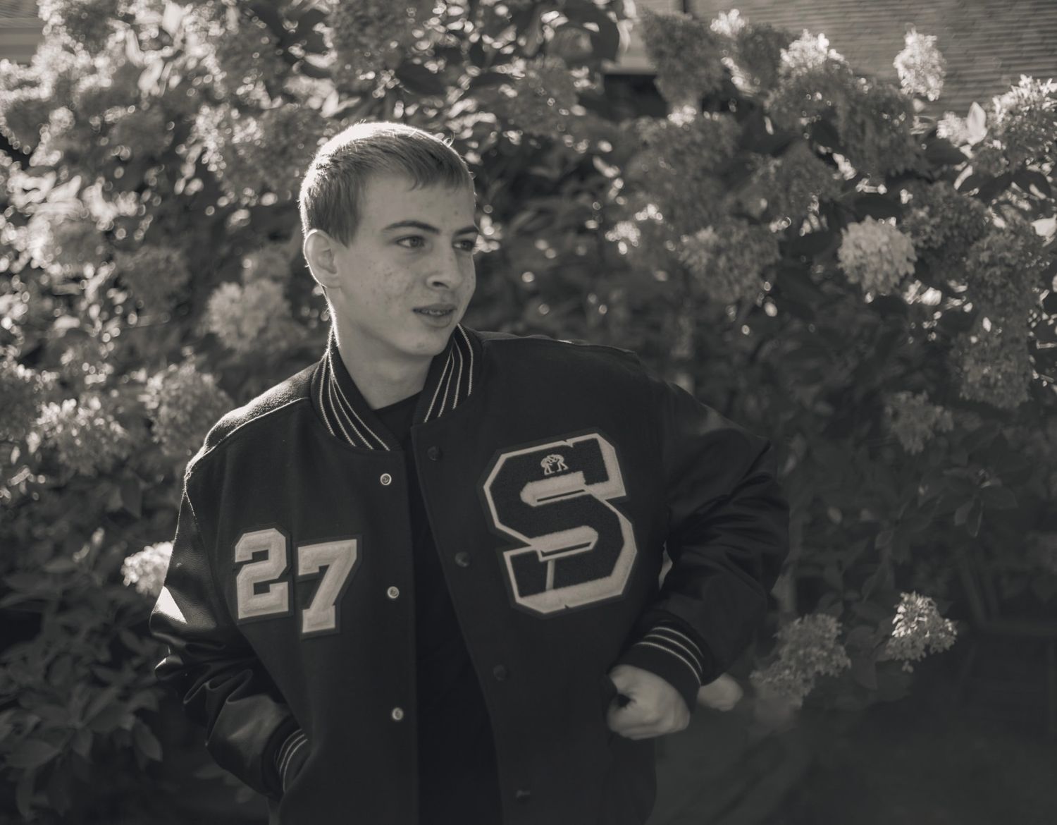 Student in varsity jacket shown in black and white outdoor portrait series.