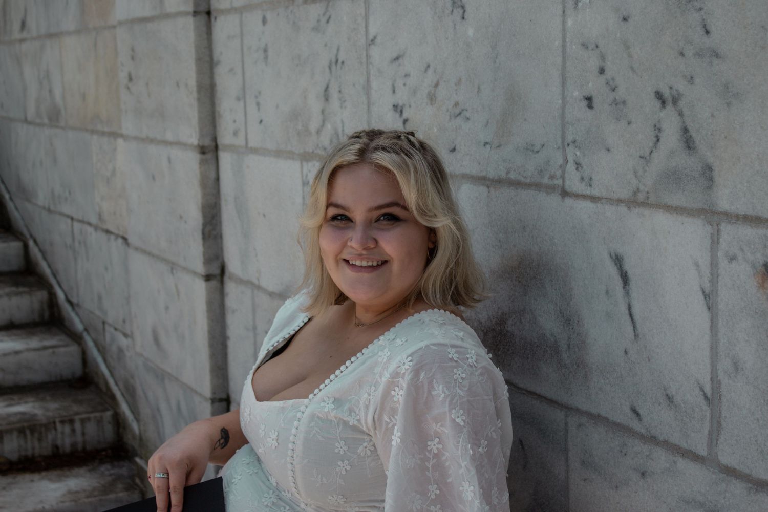 A graduate poses confidently against an industrial concrete wall background.