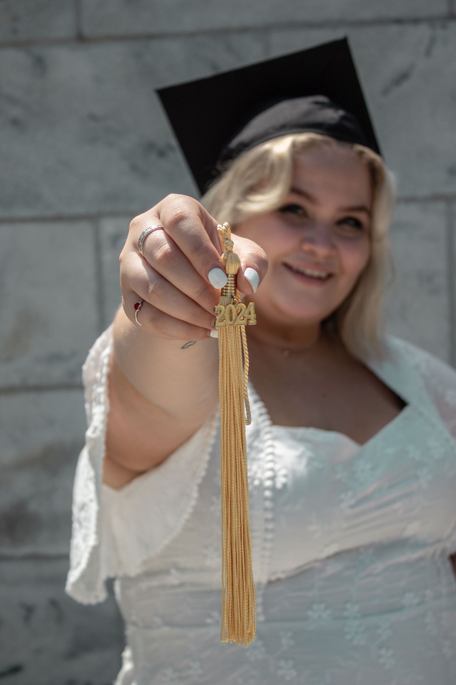 A graduate displays their gold tassel while wearing a white lace dress.