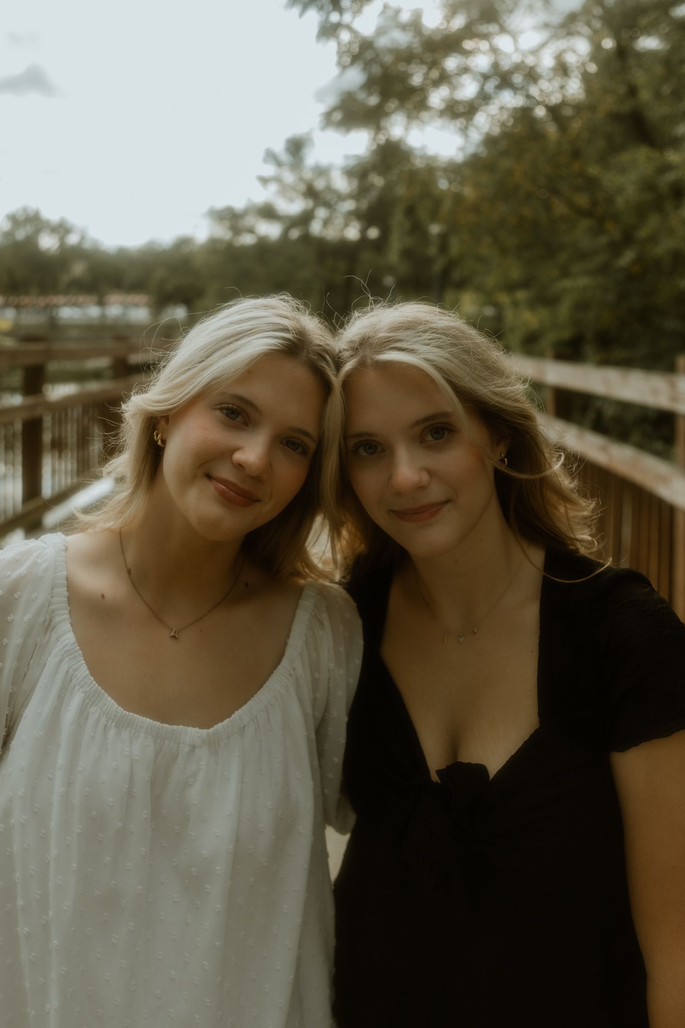 Two women in contrasting black and white outfits pose together on a wooden bridge.