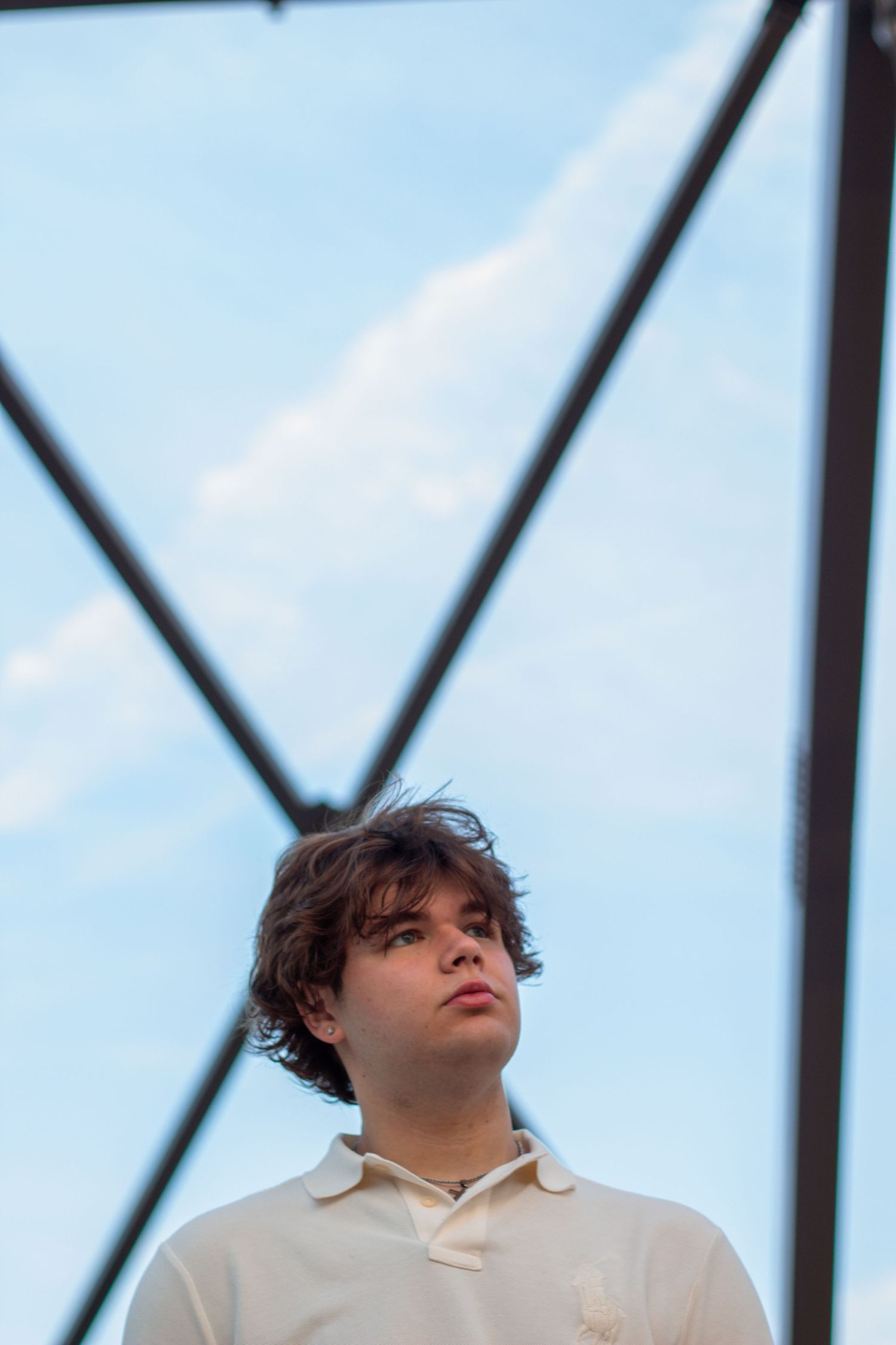 Person in white polo shirt gazing upward against geometric architectural background and blue sky.