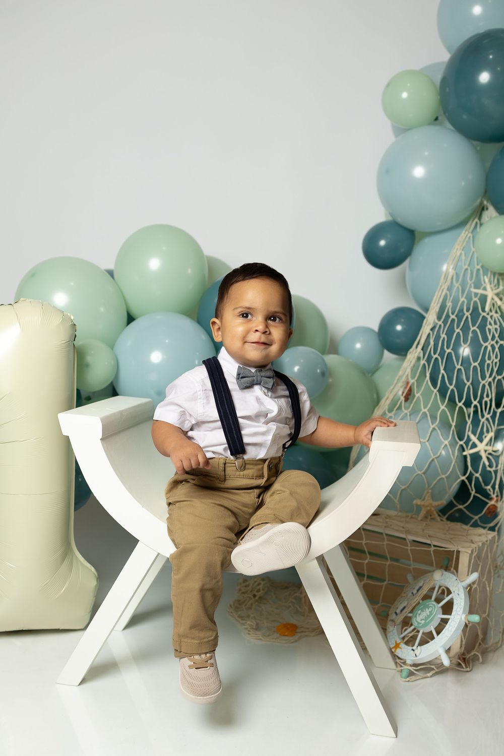 Baby photo session with white chair and soft mint and blue balloon decorations against white backdrop.